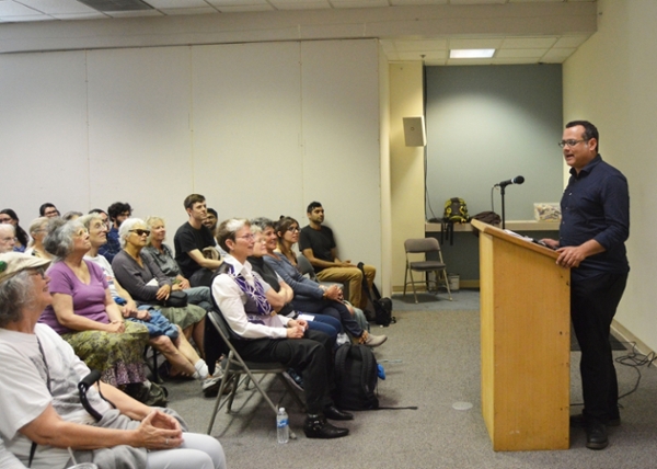 Image of Vijay Prashad speaking at a podium, with approximately 30 audience members in view.